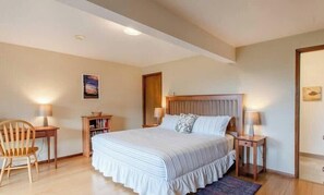 A bedroom with a large bed, wooden headboard, bedside tables, a chair, a bookshelf, and a painting on the wall. - SeaView by Manzanita Beach Getaway: Ocean View, Private Apt, Allergen-Free (Nehalem)