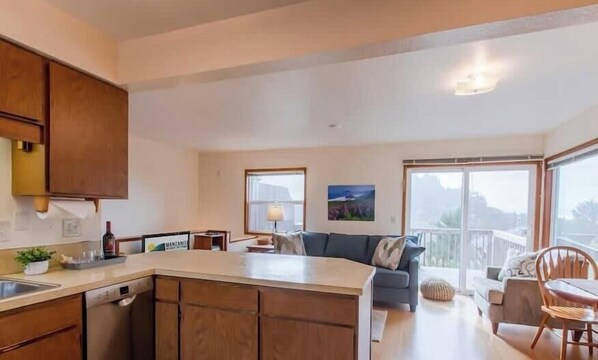 A spacious kitchen with wooden cabinets, a large island, and a dining area with a table and chairs. - SeaView by Manzanita Beach Getaway: Ocean View, Private Apt, Allergen-Free (Nehalem)