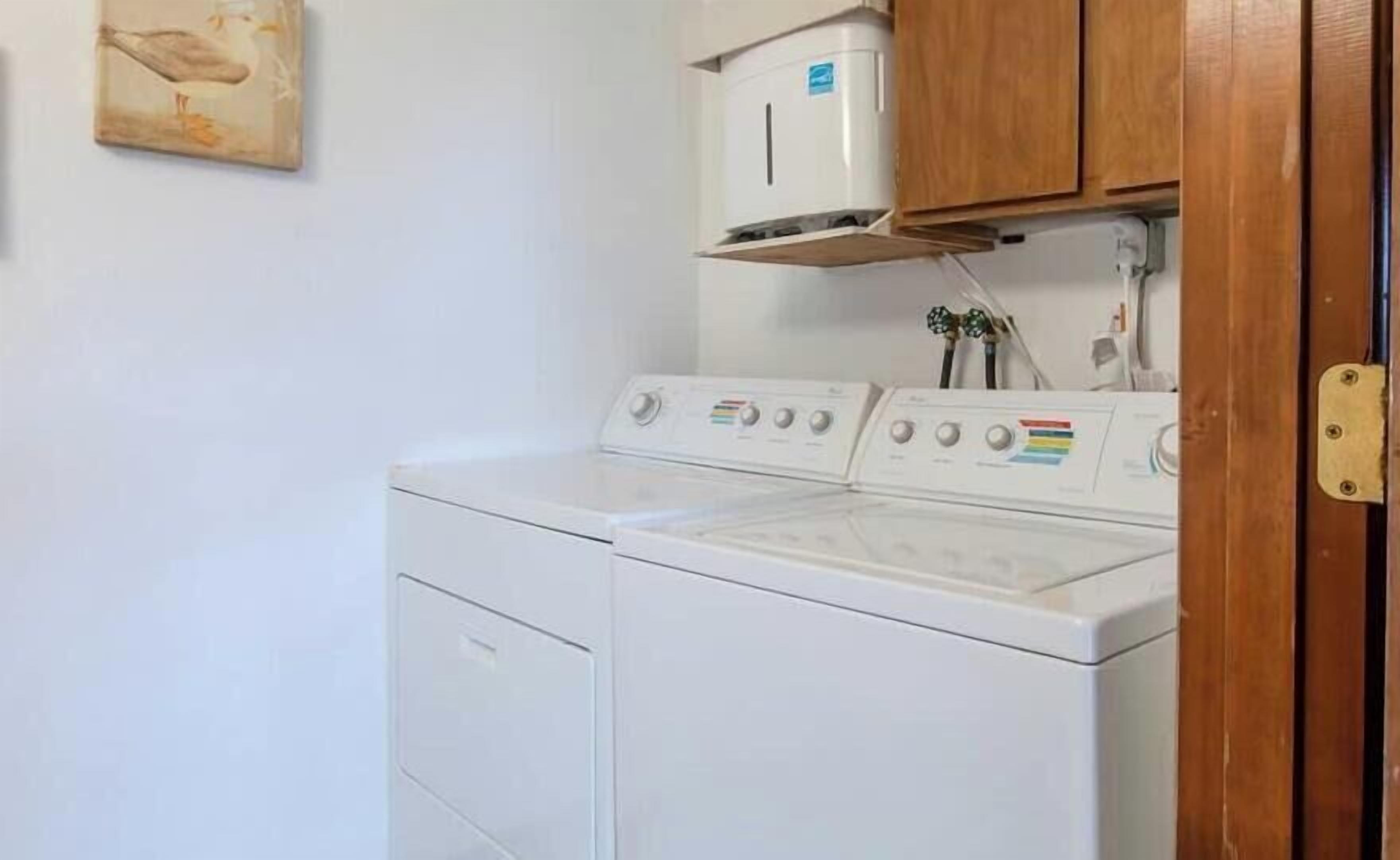 A laundry area with a front-loading washer and dryer, a wall-mounted oven, and wooden cabinets above the oven.