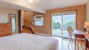 Une chambre avec un grand lit, un bureau avec une chaise, une commode et une porte-fenêtre coulissante donnant sur un balcon.