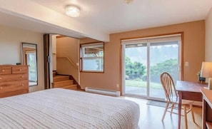 A bedroom with a large bed, a desk with a chair, a dresser, and a sliding glass door leading to a balcony. - SeaView by Manzanita Beach Getaway: Ocean View, Private Apt, Allergen-Free (Nehalem)