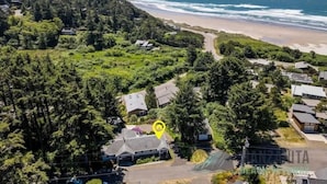 Vue aérienne d’une zone résidentielle côtière, avec des maisons, une plage et une forêt dense.