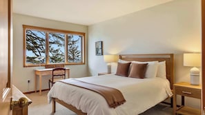 Een hotelkamer met een bed, nachtlampjes, een bureau en een raam met uitzicht op bomen.