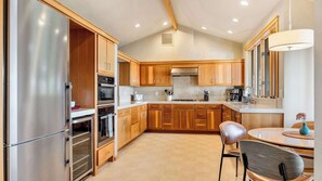 Une cuisine moderne avec des meubles en bois, des appareils électroménagers en acier inoxydable et un coin repas comprenant une table et des chaises.