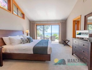 A hotel room with a bed, a TV, a desk, and a view of the sea.