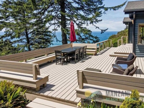 A wooden deck with a table and chairs, a red umbrella, and a view of the ocean.