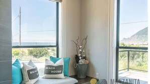 A balcony with a cushioned seating area, decorative pillows, a small potted plant, and a view of the landscape. - Light House by Manzanita Beach Getaway: High-End w/ Ocean & Neahkahnie Views (Manzanita)