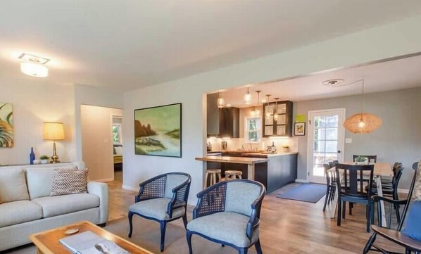 A modern living room with a sofa, two armchairs, a coffee table, and a dining area with a table and chairs.