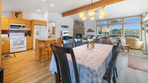 A modern kitchen with wooden cabinets, a dining area with a floral tablecloth, and a fireplace. - Coastal View by Manzanita Beach Getaway: Ocean Views, Dog-Friendly & Great Deck (Neahkahnie)