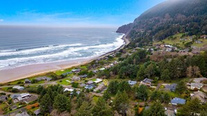 A coastal residential area with houses, a beach, and a forested hillside. - Coastal View by Manzanita Beach Getaway: Ocean Views, Dog-Friendly & Great Deck (Neahkahnie)