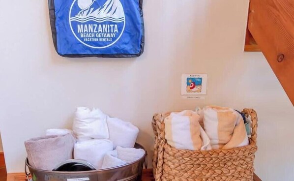 A room with a wall-mounted towel rack holding white towels, a woven basket with towels, and a blue bag with a beach-themed logo.