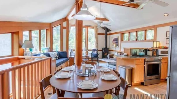 Un vaste espace dédié à la salle à manger, avec une table ronde prévue pour quatre personnes, un plancher en bois et de grandes fenêtres laissant entrer la lumière naturelle.