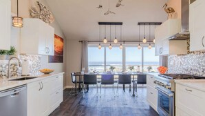 Een moderne keuken met witte kasten, een eethoek met uitzicht op zee en een groot raam.