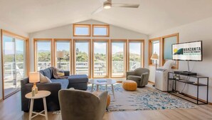 Un soggiorno spazioso con una grande finestra, una ventola a soffitto e un televisore che mostra 'Manzanita Beach Getaway Vacation Rentals'.