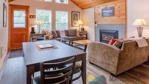 Un salon chaleureux avec une cheminée, un plafond en bois et un coin repas comprenant une table et des chaises.