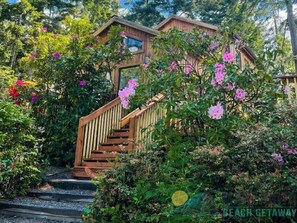 A wooden staircase leading to a house surrounded by lush greenery and pink flowers.
