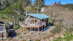 Eine zweistöckige Holzhütte mit Balkon, umgeben von Bäumen und blauem Himmel.