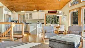 A modern kitchen with wooden cabinets, a dining area with chairs, and a view of trees through large windows. - Legasea on the Pond by Manzanita Beach Getaway: Dog-Friendly, Scenic Views (Nehalem)
