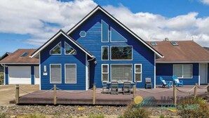 Une maison bleue à deux étages, dotée d’un patio couvert, d’un garage et d’une petite terrasse avec des chaises.