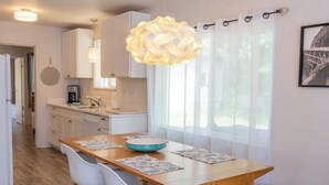 Una cocina moderna con armarios blancos, una mesa de comedor de madera con individuales, y una lámpara colgante.