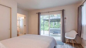 Un dormitorio con cama, una silla y un ventanal corredero que da a un espacio al aire libre.