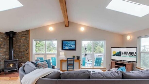 Una sala de estar acogedora con pared de piedra, chimenea, sofá y una pantalla de televisión que muestra 'Manzanita Beach Getaway Vacation Rentals'.