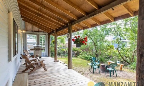 A covered porch with wooden flooring, outdoor seating, and hanging flowers.