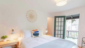 Un dormitorio con cama, mesitas de noche, lámpara, reloj de pared y puerta que da a un área exterior.