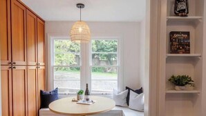 Una habitación acogedora con una mesa redonda, una lámpara colgante y vistas al exterior con vegetación.