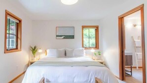 Un dormitorio con una cama grande, dos mesitas de noche con lámparas, un cuadro en la pared y una ventana con vistas a árboles.