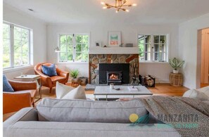 A cozy living room with a fireplace, comfortable seating, and large windows. - Gingerbread Haus by Manzanita Beach Getaway: Fenced Yard, Hot Tub, Near Beach (Nehalem)
