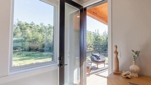 Ein modernes Zimmer mit großem Fenster, Holzboden und Blick auf einen Balkon mit Sitzmöbeln.