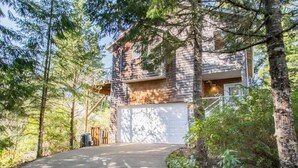 Une maison à deux étages avec un garage, entourée d’une forêt dense.
