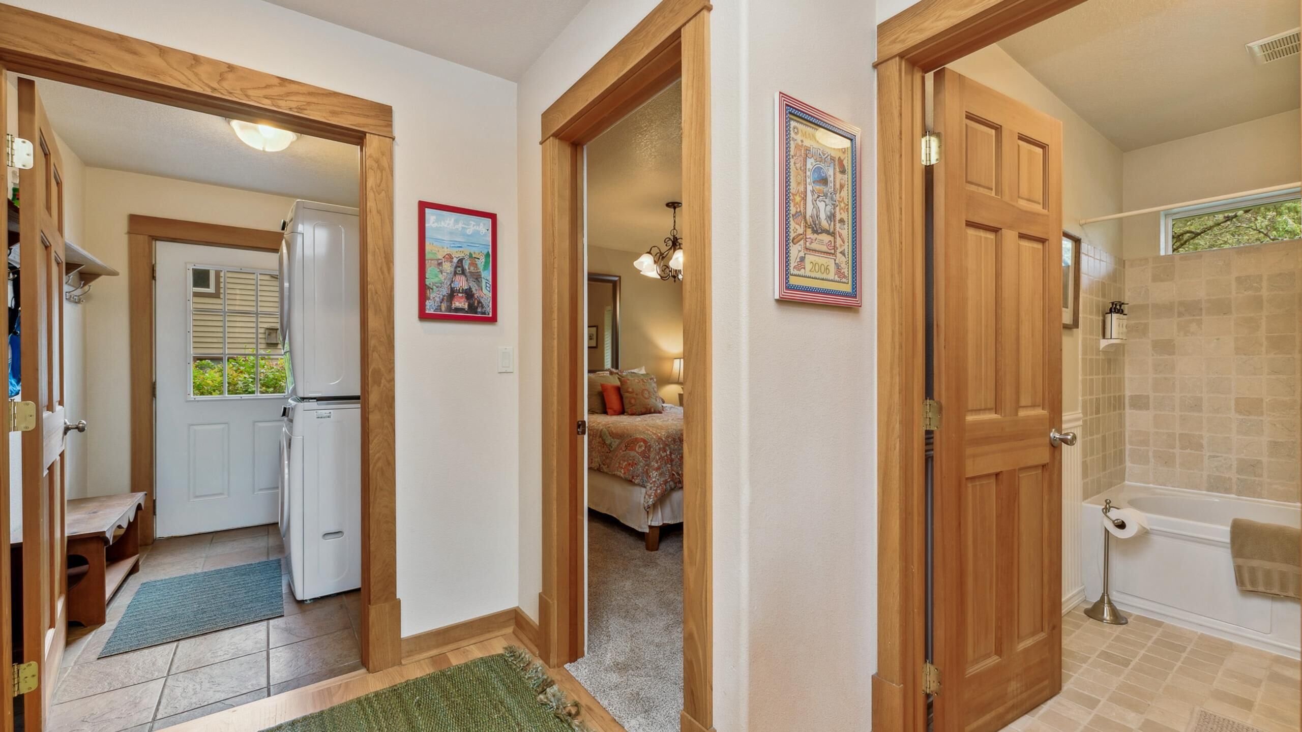 A hallway with a refrigerator, a door leading to a bedroom, and a bathroom with a bathtub.