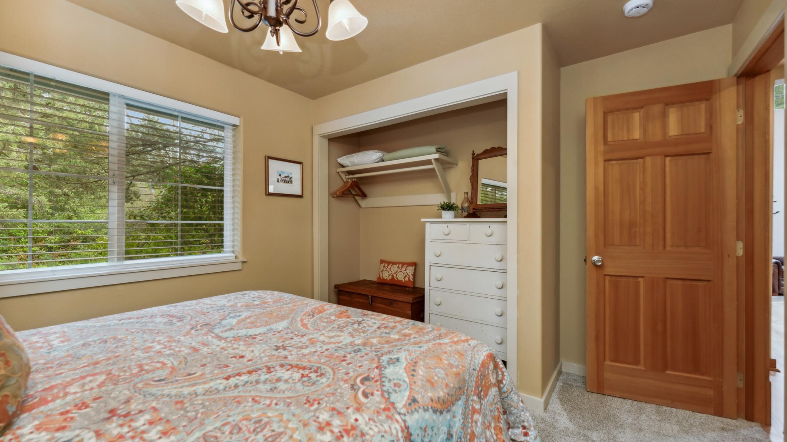 Een slaapkamer met een bed, een dressoir, een kast en een deur.