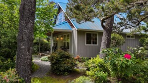 Ein Haus mit geneigtem Dach, einer Veranda und einem Garten mit verschiedenen Pflanzen und einer roten Blume.