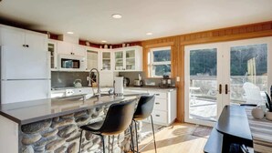 A modern kitchen with a stone island, two bar stools, and a dining table with chairs.