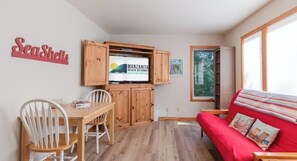 A cozy room with a wooden dining table, a red sofa, and a TV displaying 'Manzanita Beach Getaway Vacation Rentals'.