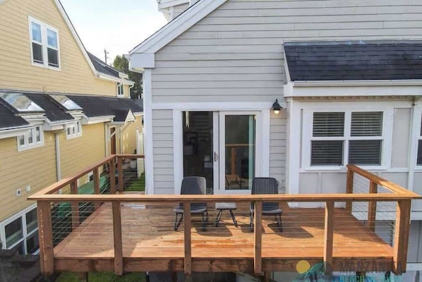 Une terrasse en bois avec des sièges d’extérieur, une porte-fenêtre coulissante et un petit espace porche.