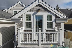 Une maison avec un toit à pignon, un porche à l’avant avec des balustrades blanches et une fenêtre avec des volets.