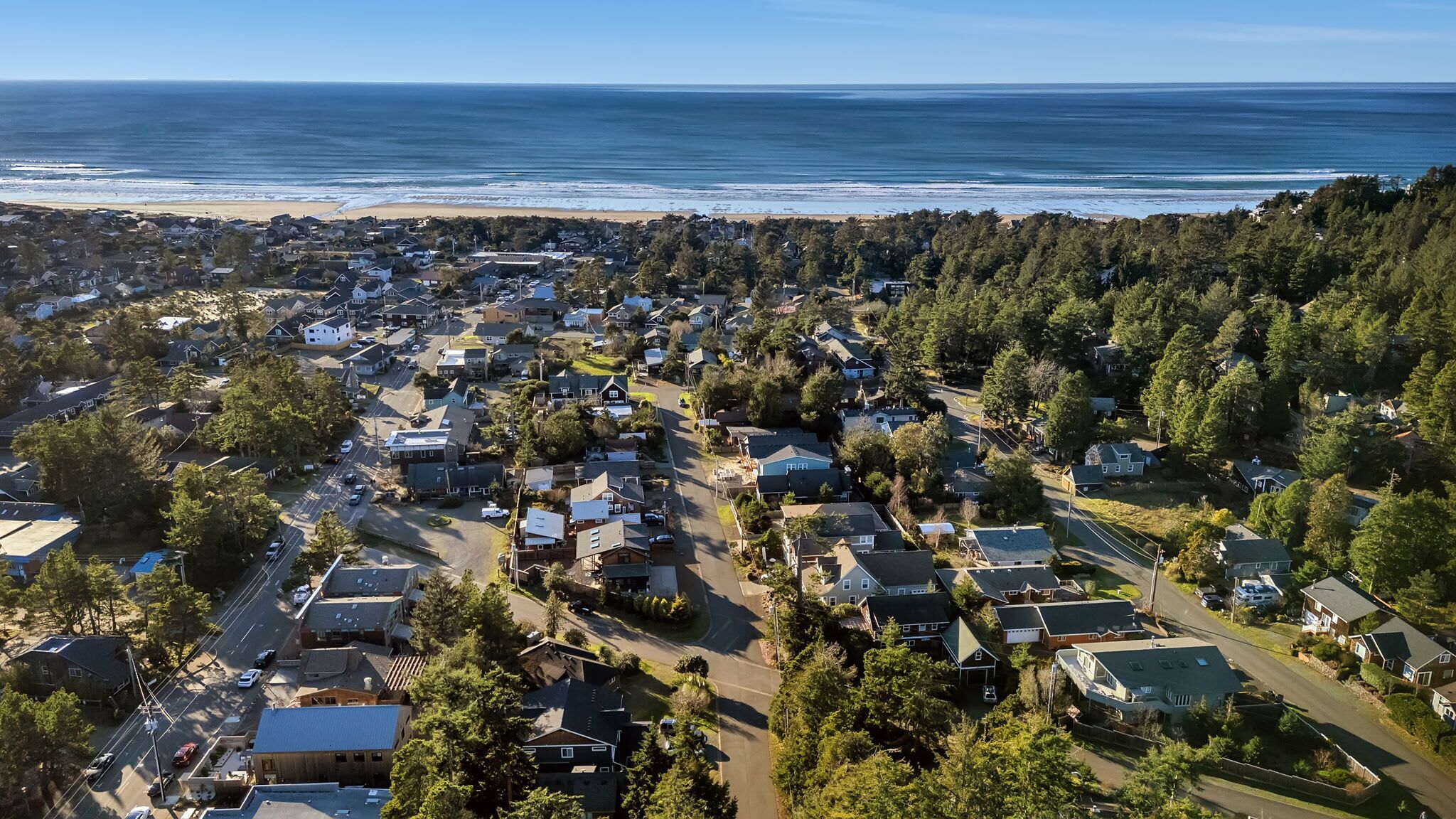 An aerial view of a residential area with houses, roads, and a beach in the background.
