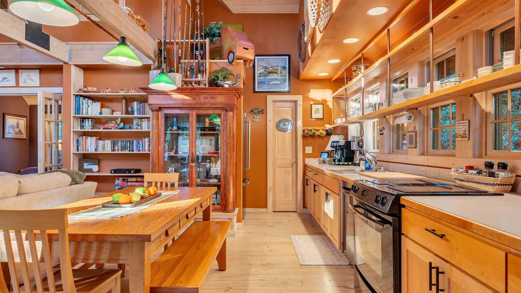 A cozy kitchen with wooden cabinets, a dining area with a bench, and a bookshelf filled with books and toys.