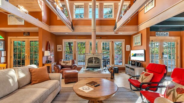 Un salón amplio con chimenea, sofás de cuero, televisión y ventanas grandes que ofrecen vistas al exterior.