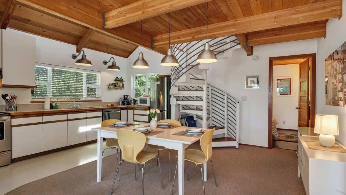 Une cuisine moderne avec des poutres en bois, un coin repas avec des chaises jaunes et un escalier en colimaçon.