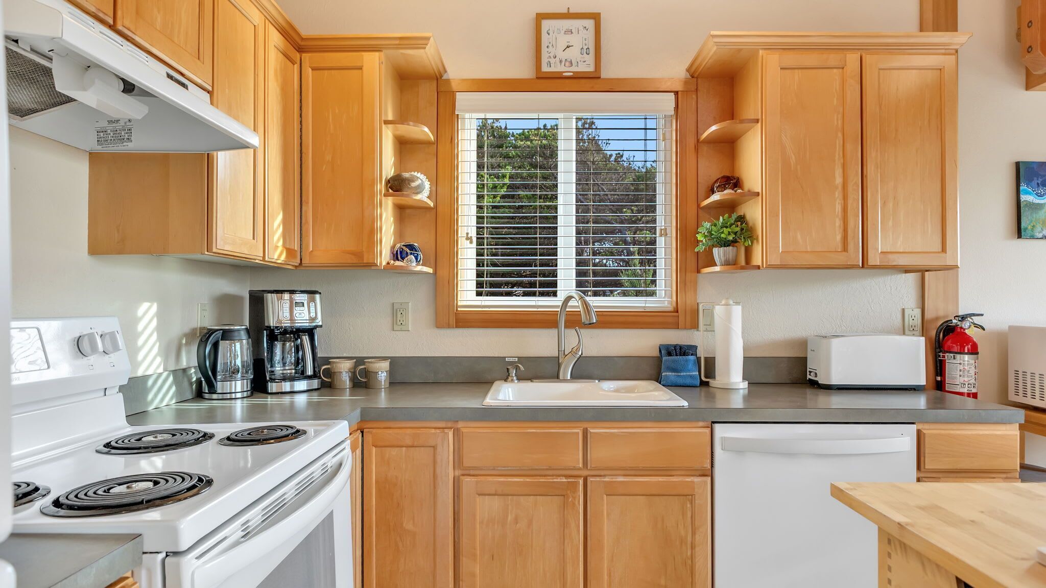 A compact kitchen with wooden cabinets, a stove, a coffee maker, a sink, and a toaster.