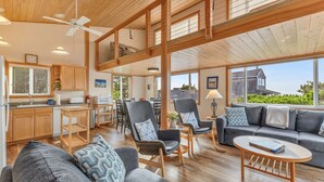 A spacious living area with a high ceiling, wooden beams, a dining area, and a view of the outside. - Forever Manzanita by Manzanita Beach Getaway: Ocean View, Dog-Friendly, Hot Tub (Manzanita)