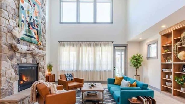 A spacious living room with a stone fireplace, a large window, a blue sofa, and a bookshelf.