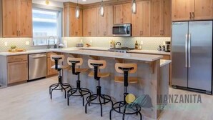 A modern kitchen with wooden cabinets, stainless steel appliances, and bar stools.