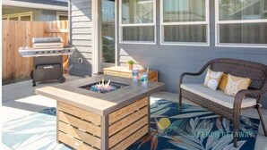 An outdoor patio area with a built-in grill, a fire pit, and a wicker chair.