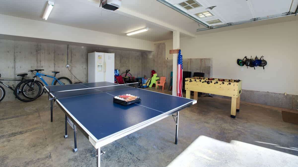 A room with a ping pong table, bicycles, a foosball table, and helmets on the wall.